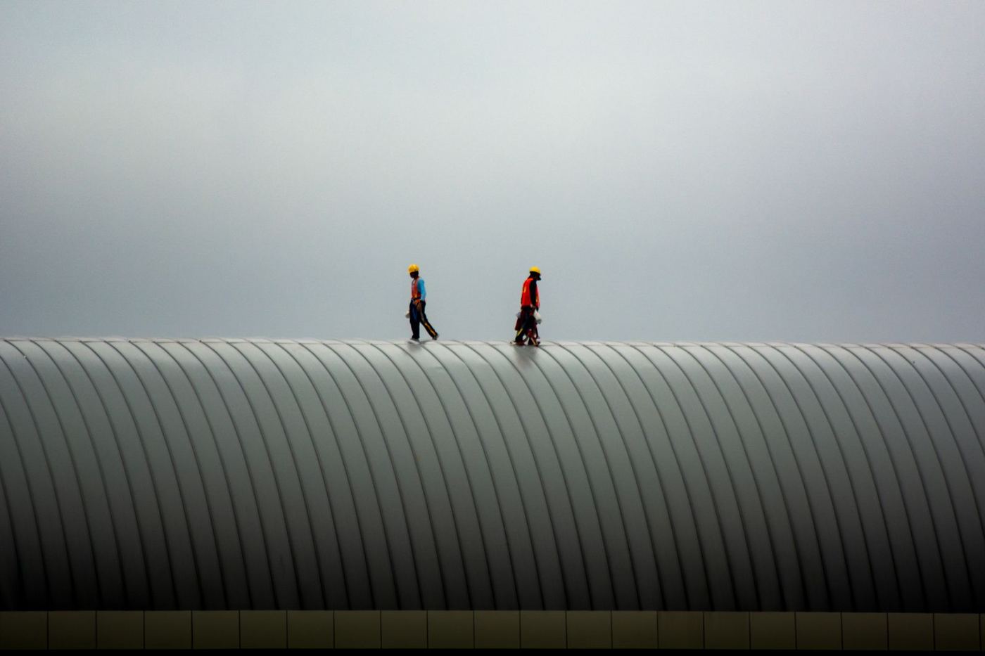 Two roofers walking a curved metal roof