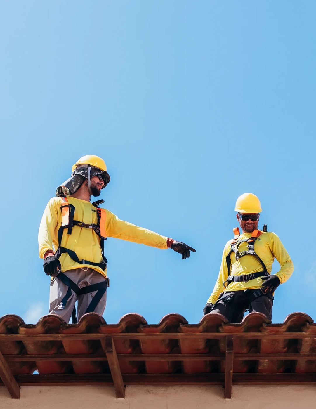 Two roofers in safety gear on a tile roof